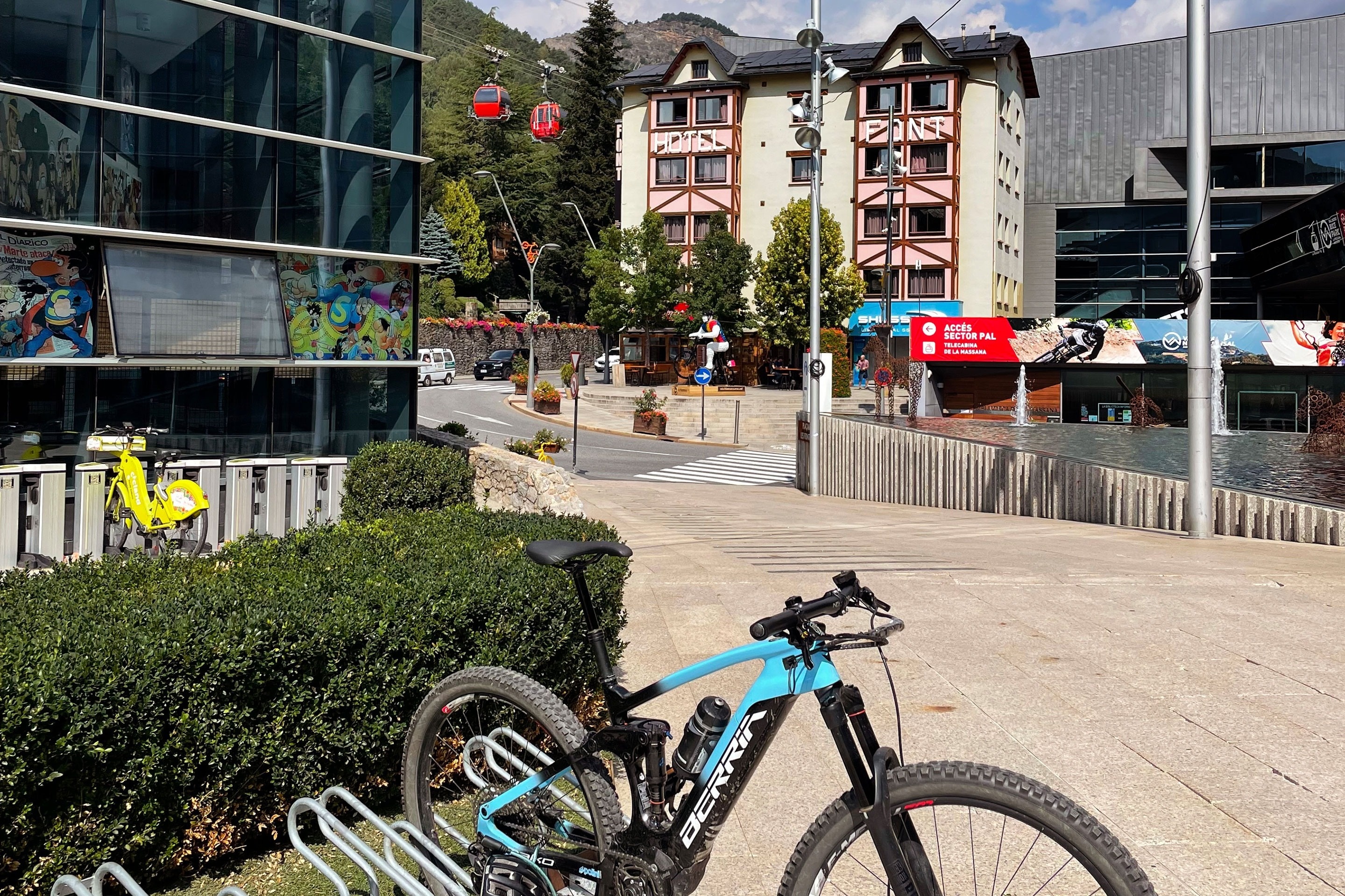 un vélo de montagne bleu et noir est garé devant un bâtiment avec un téléphérique en arrière-plan