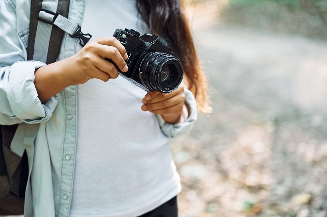 una mujer con una mochila sostiene una cámara con una lente de 50 mm