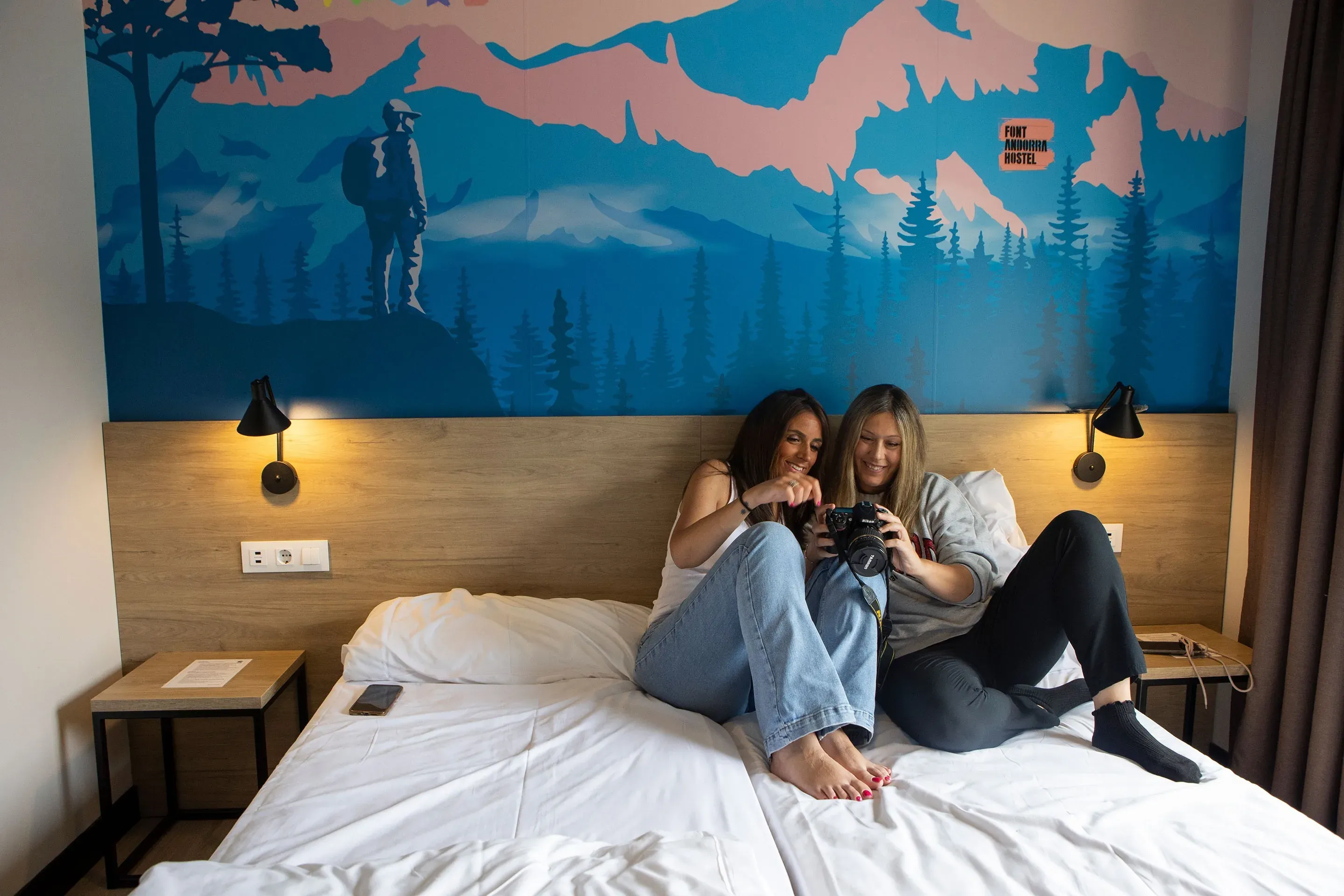 Deux amies regardent des photos sur un appareil photo dans une chambre d'hôtel à Font Andorra Auberge | Nexta | Site Officiel.