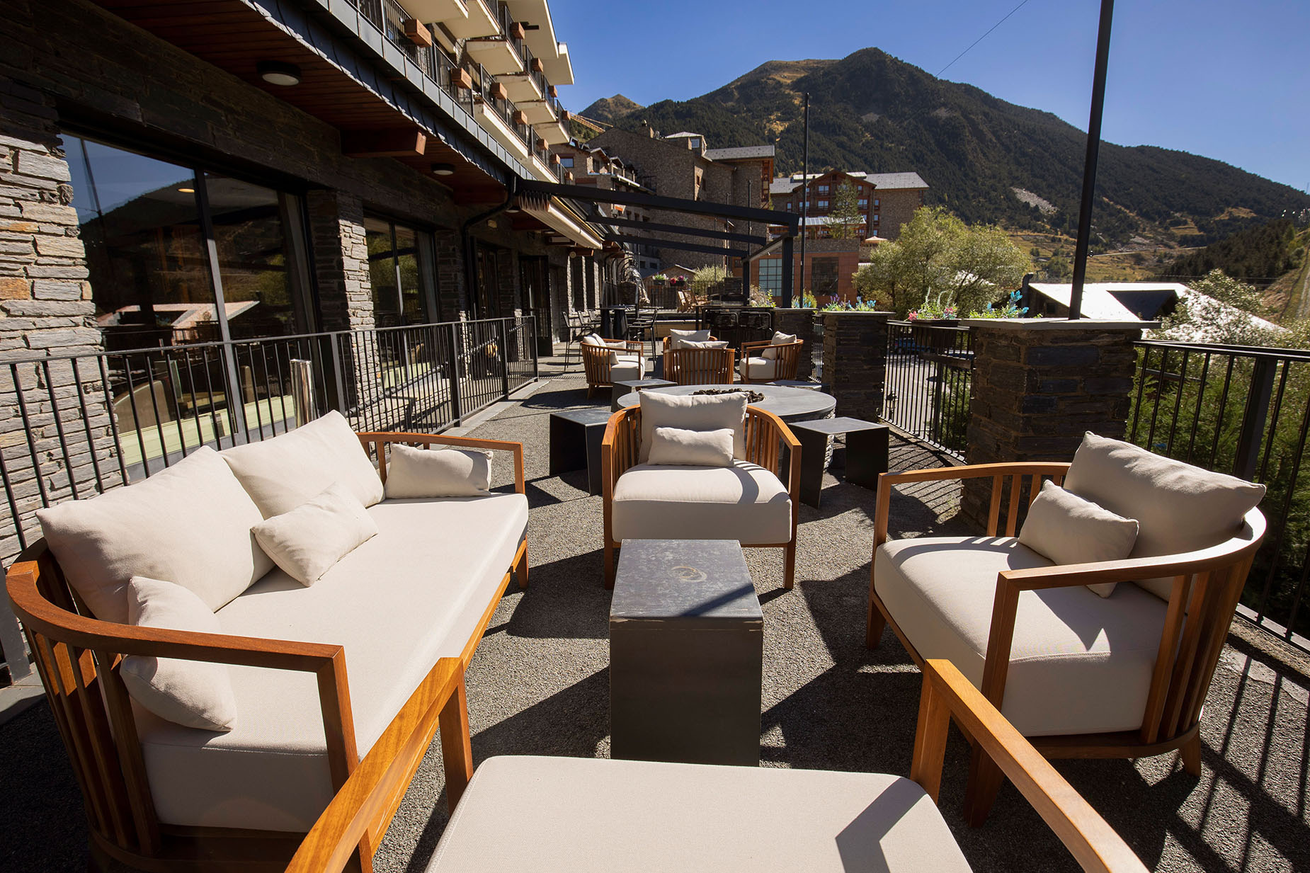 Terraza exterior de hotel NEXTA: Corporativa con sofás y sillones de madera y montaña de fondo.