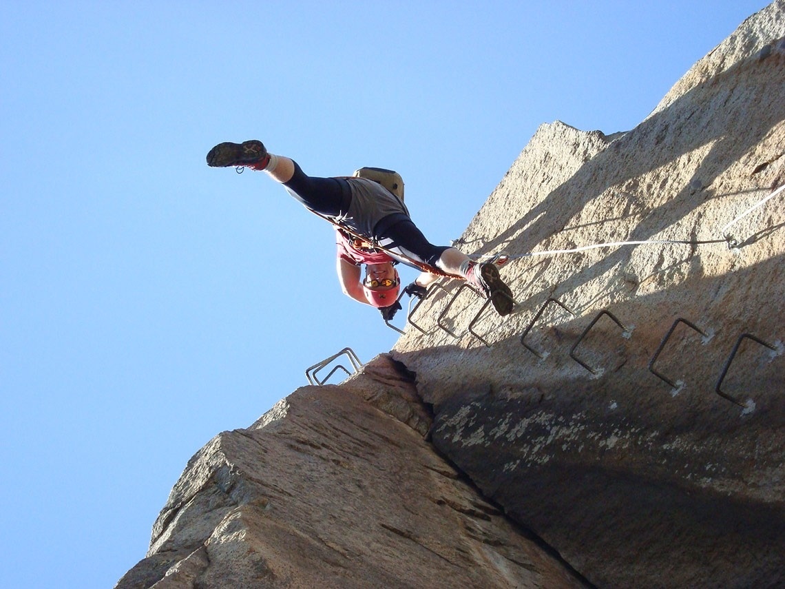 a person wearing a red helmet and black shorts is climbing a rock wall