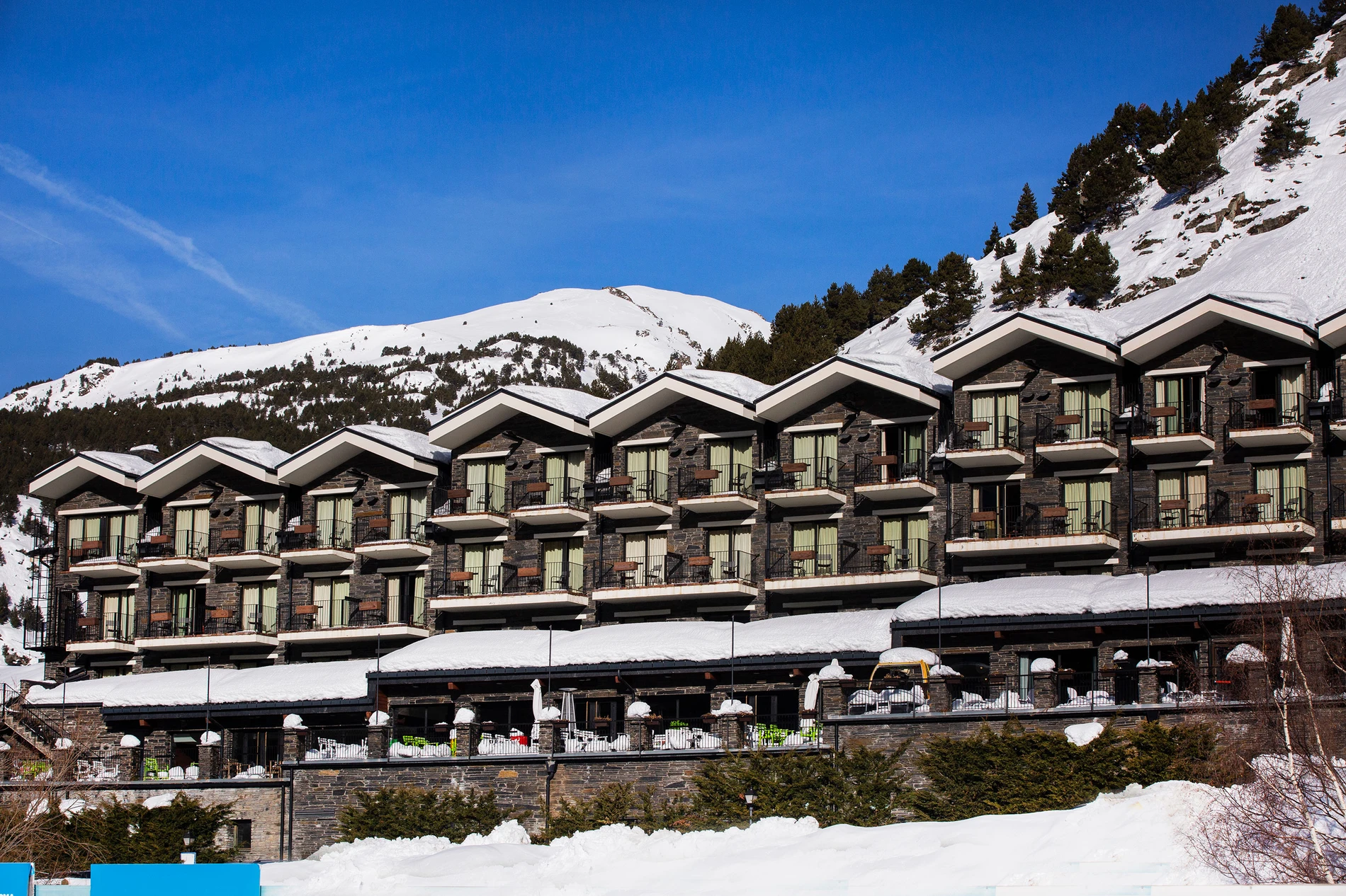 Hotel Piolets Soldeu Centre | Nexta | Web Oficial: hotel de montaña con balcón, frente a pistas nevadas y cielos azules.