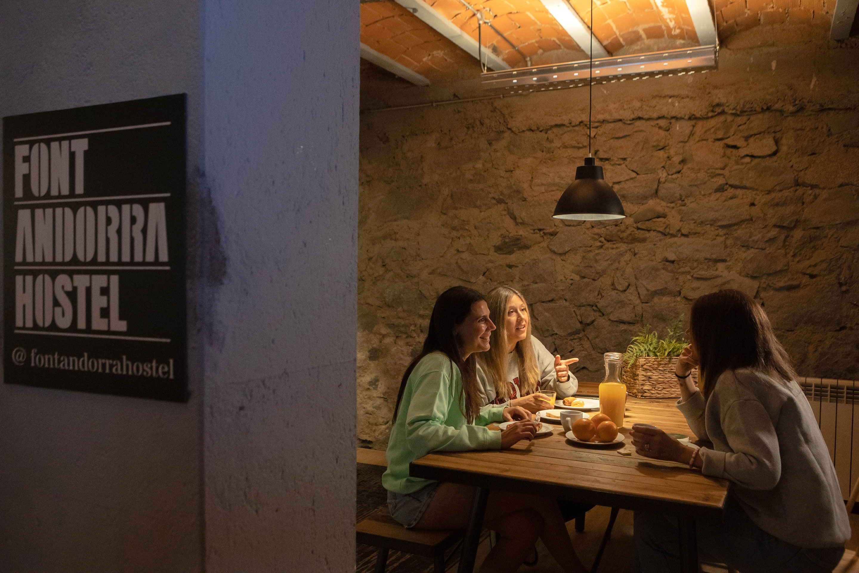 trois jeunes femmes sont assises à une table à côté d' un panneau qui dit font andorra hostel