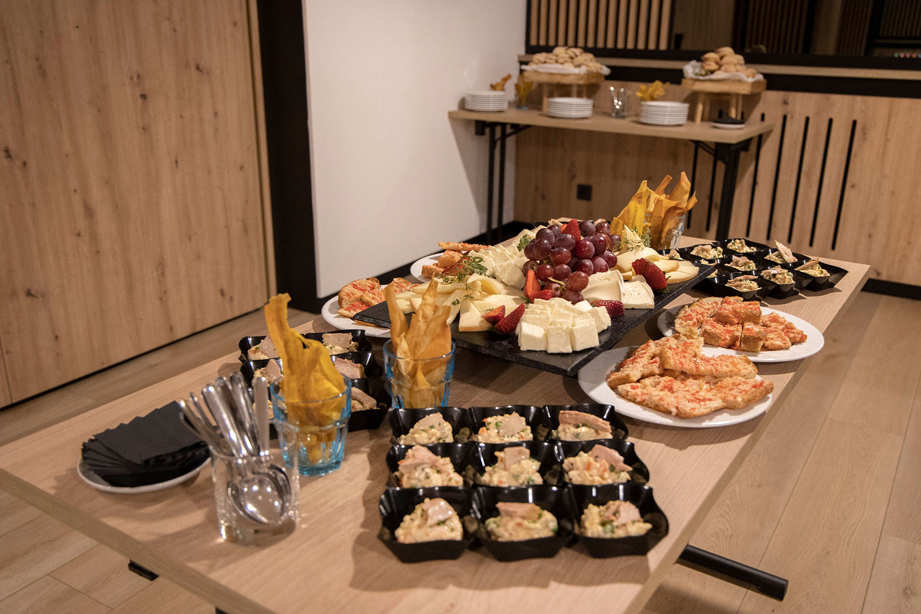 Buffet NEXTA: Corporativa: cheese board, grapes, strawberries, pizza, and appetizers served on a wooden table.
