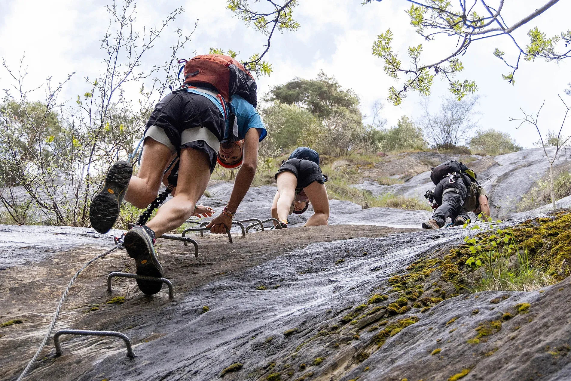 a man with a blue backpack helps a woman climb a mountain