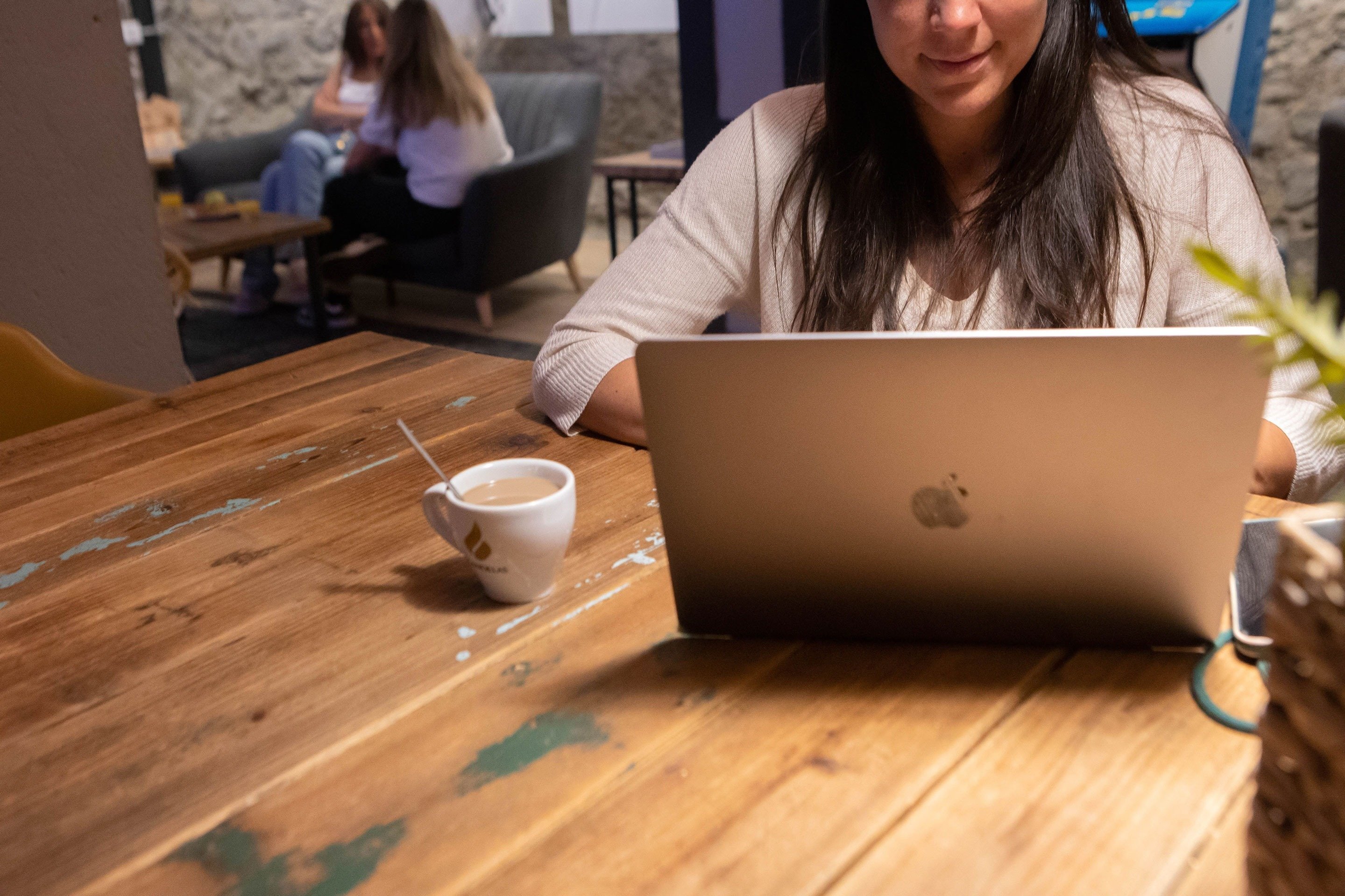 una mujer se sienta en una mesa con una computadora portátil y una taza de café