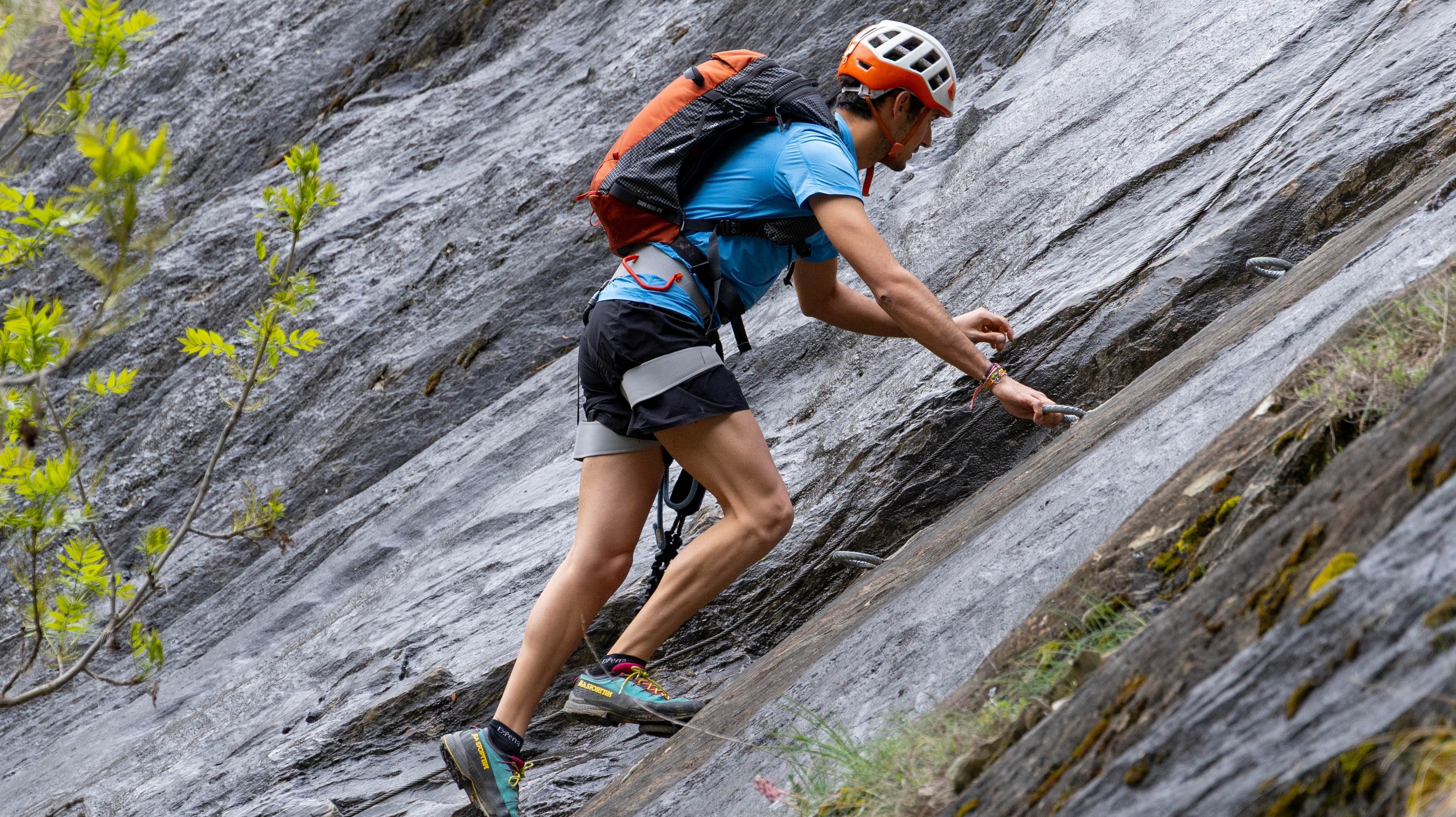 una mulher usando um capacete preto e laranja está escalando uma parede de pedra
