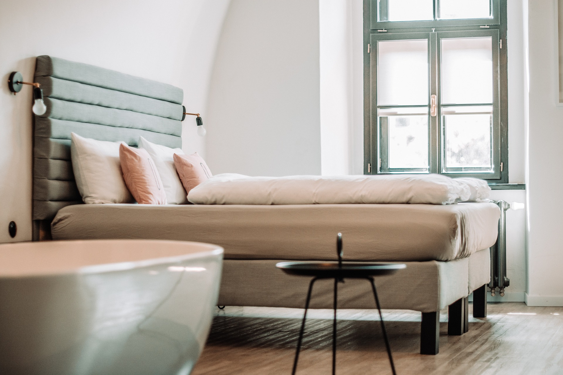 Comfortable bed with plush pillows and a bathtub in a modern hotel room. NEXTA: Corporativa