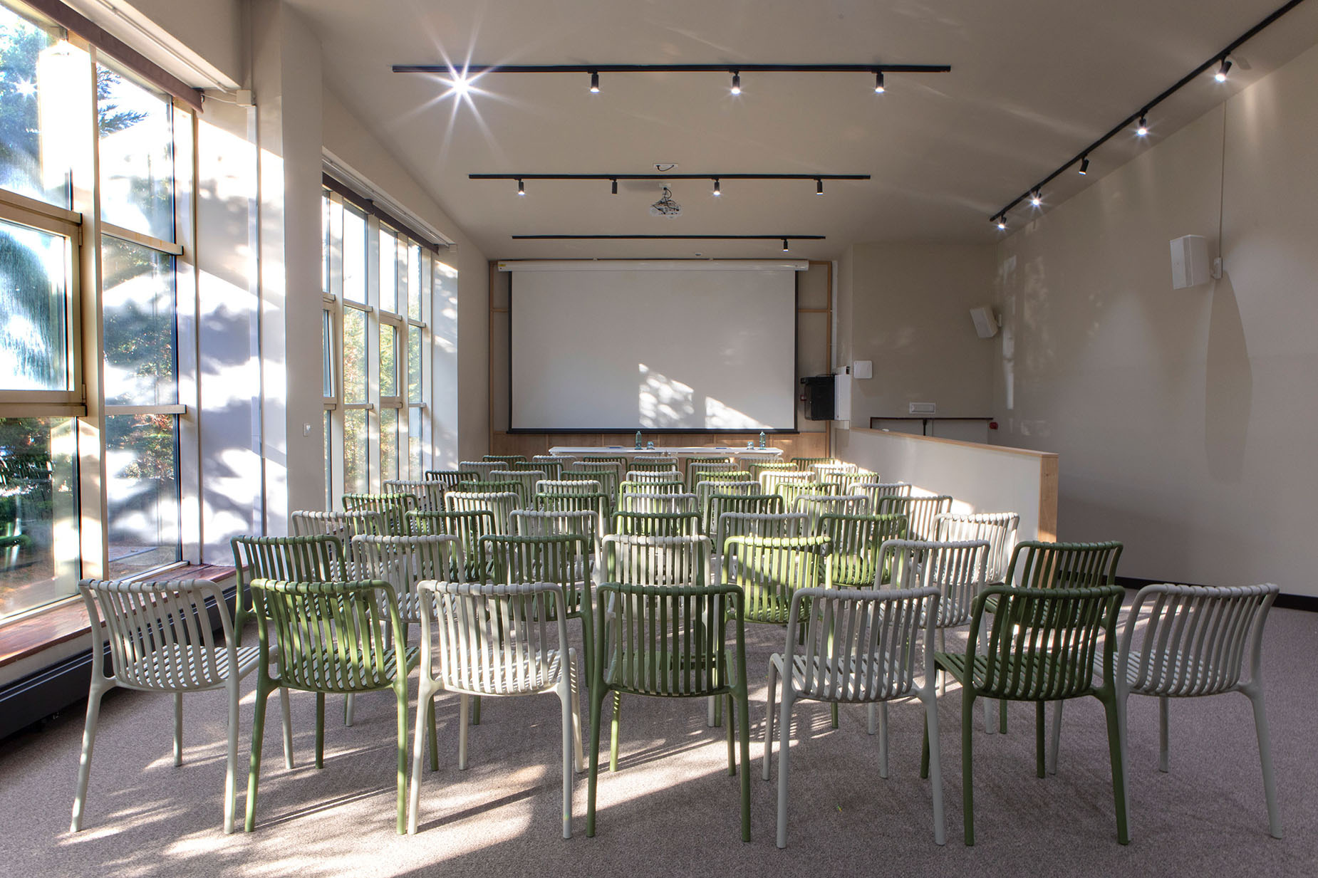 Sala de conferencias moderna con sillas verdes y blancas, proyector y luz natural NEXTA: Corporativa.