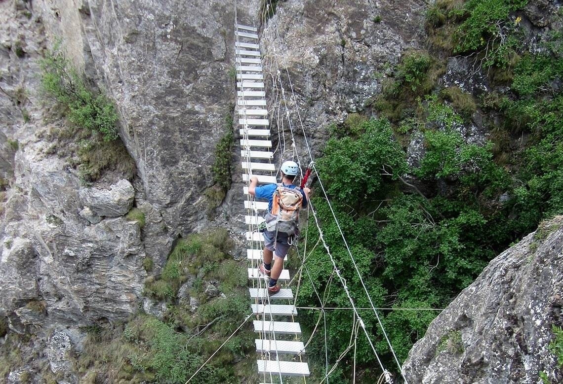 two people are walking across a suspension bridge in the mountains