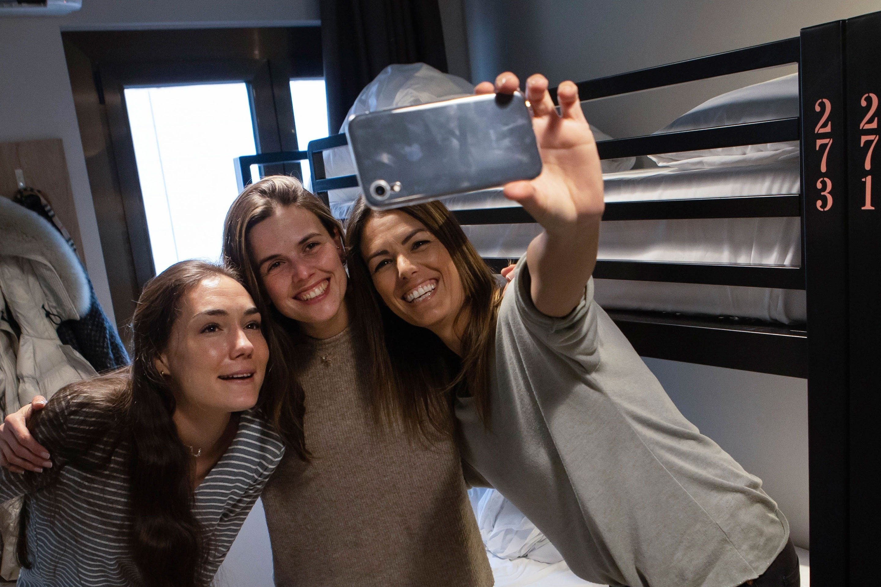 tres mujeres se toman un selfie en una habitación con literas con los números 27 31