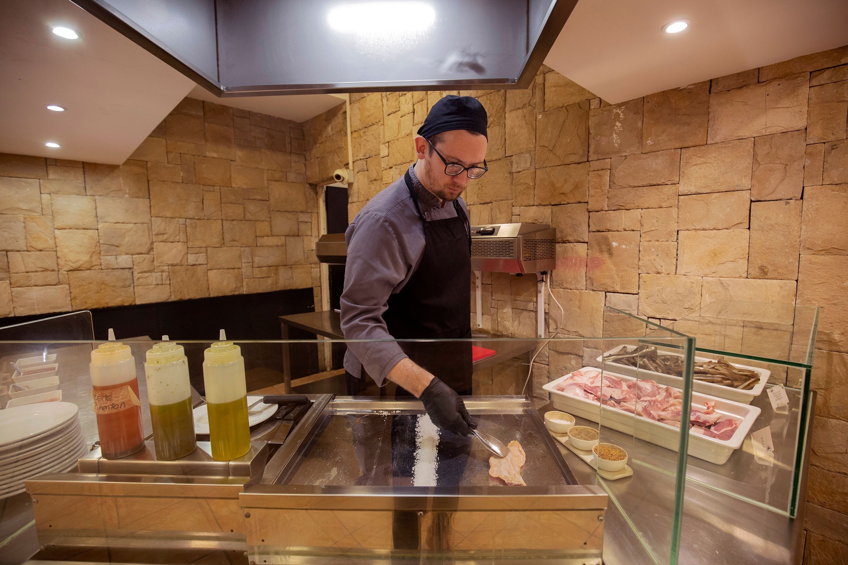 un chef prépare une nourriture dans une cuisine avec des bouteilles de sauces à côté de lui