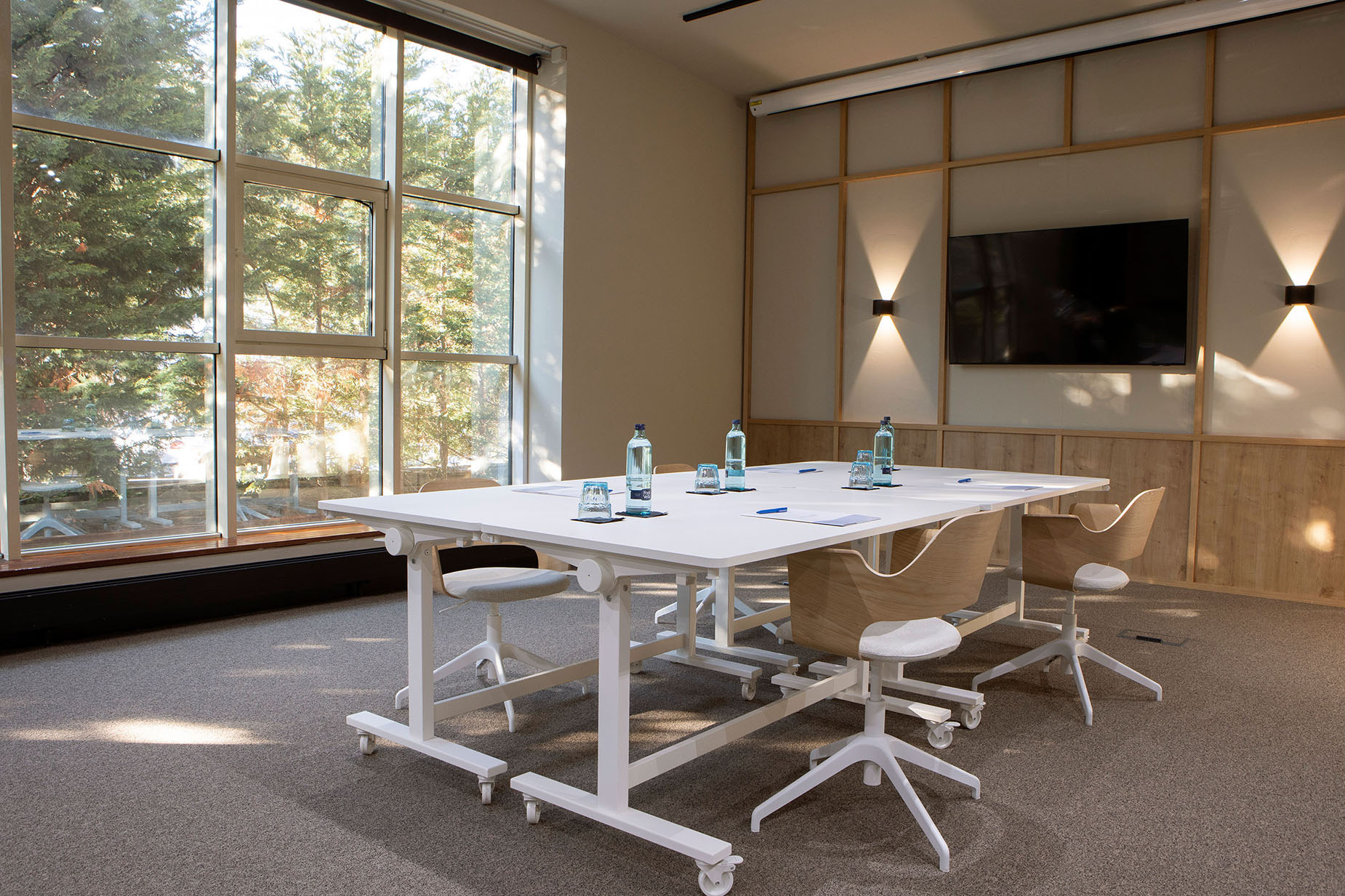 Sala de conferencias moderna con mesa, sillas y vistas a la naturaleza, ideal paraNEXTA: Corporativa
