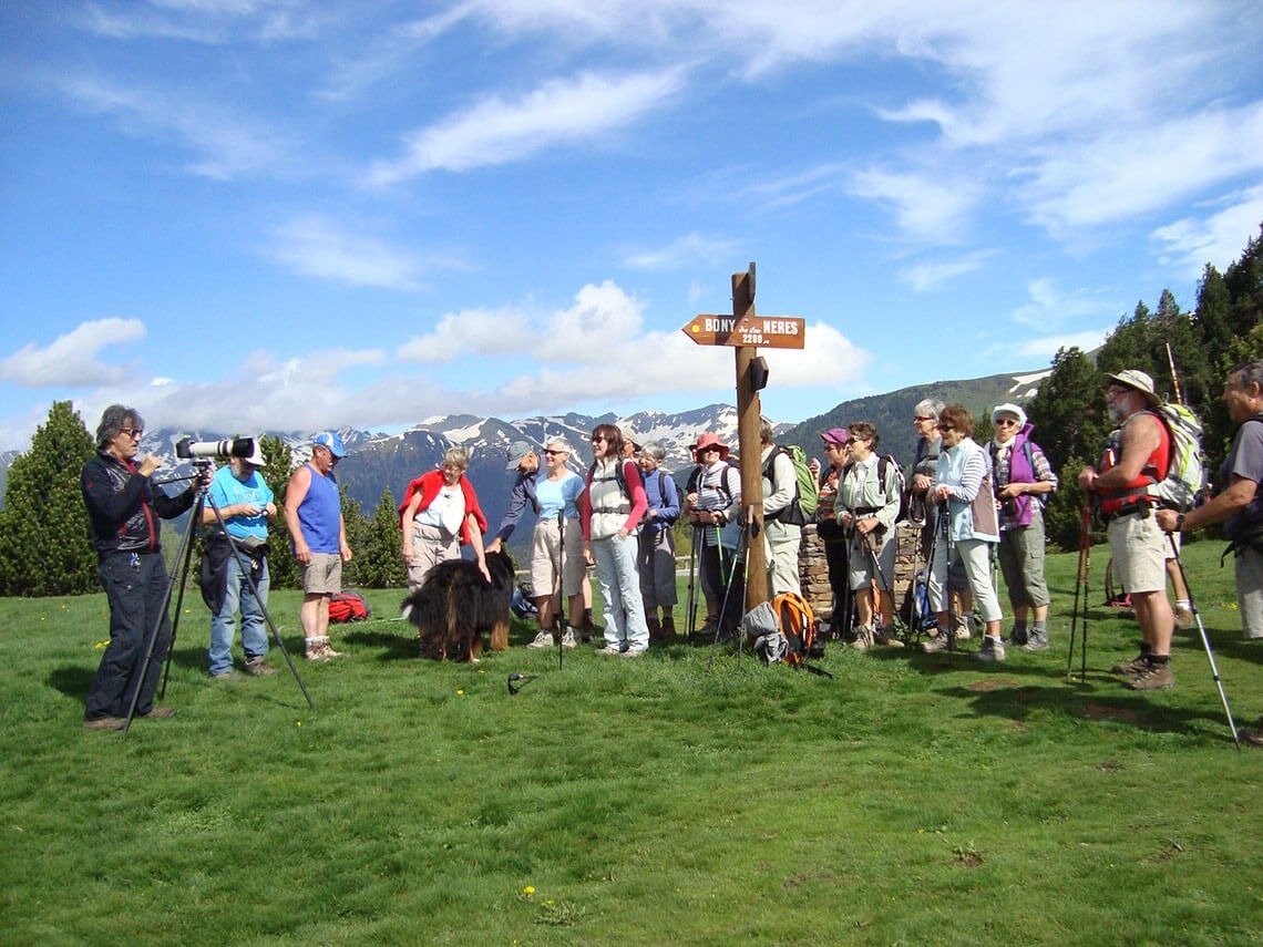 un grupo de excursionistas se reúnen alrededor de un poste de madera con una flecha que apunta hacia la derecha