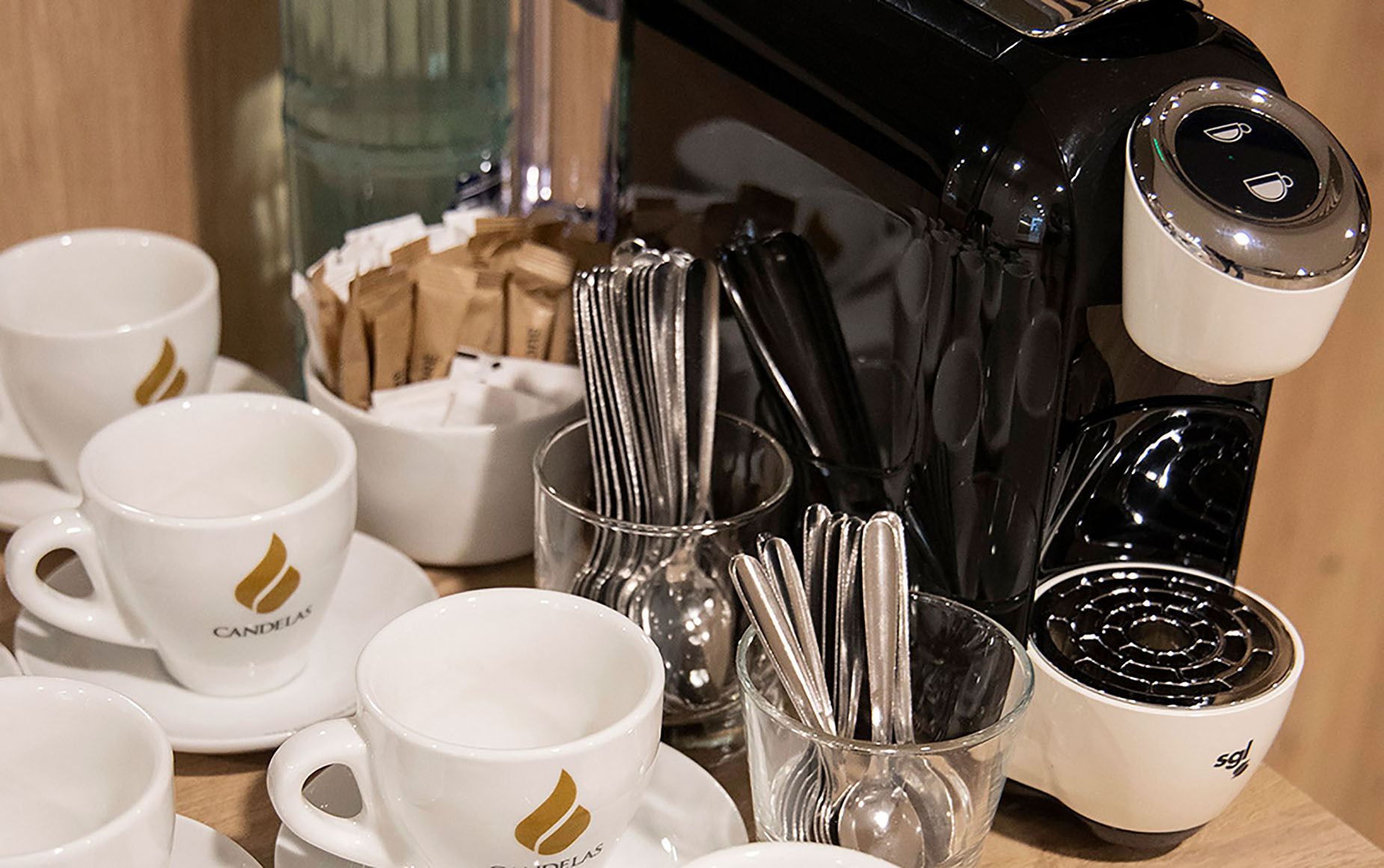 Hotel coffee station with cups, sugar packets, and a coffee machine. NEXTA: Corporativa