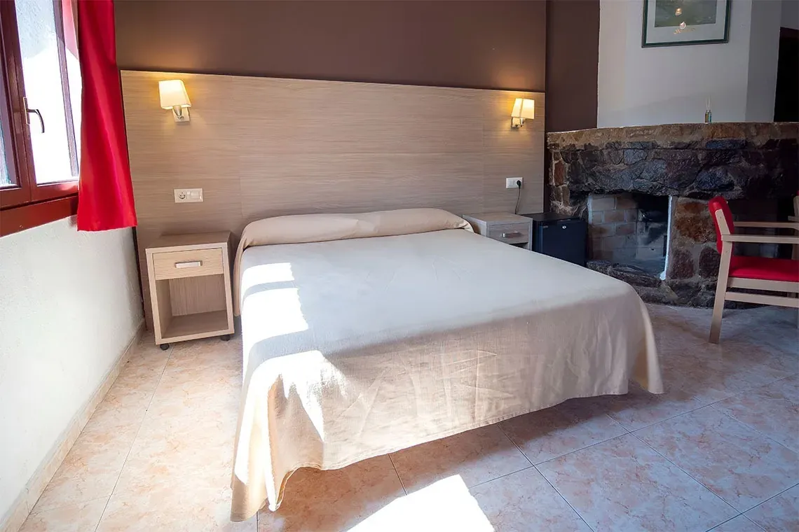 Chambre confortable avec cheminée en pierre, lit NEXTA: Corporativa et lumière naturelle.