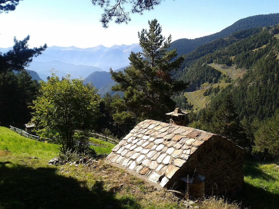 una cabaña de piedra en medio de un bosque con montañas en el fondo
