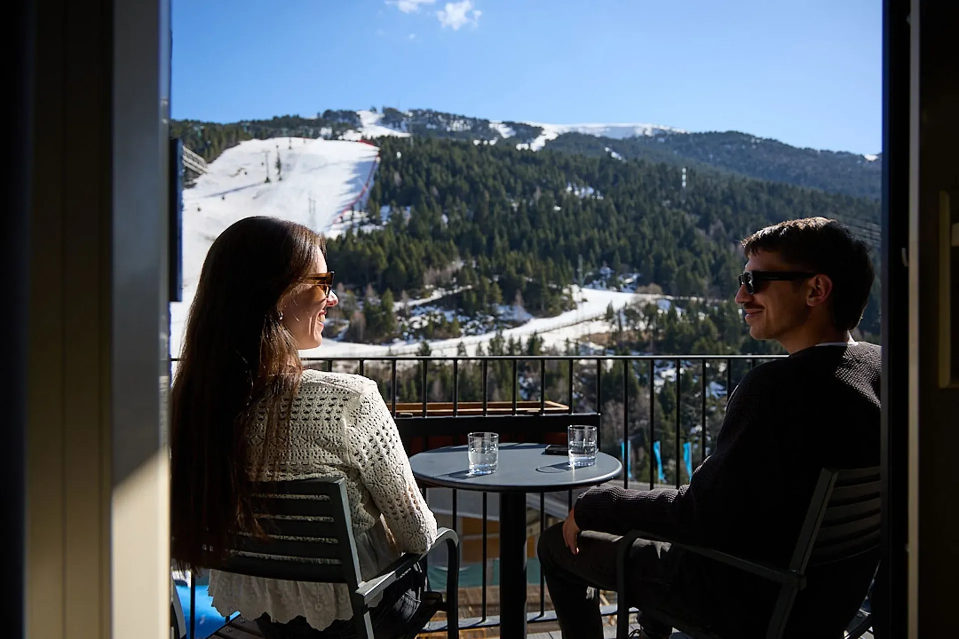 Couple enjoying NEXTA: Corporativa view from balcony with snowy mountains.