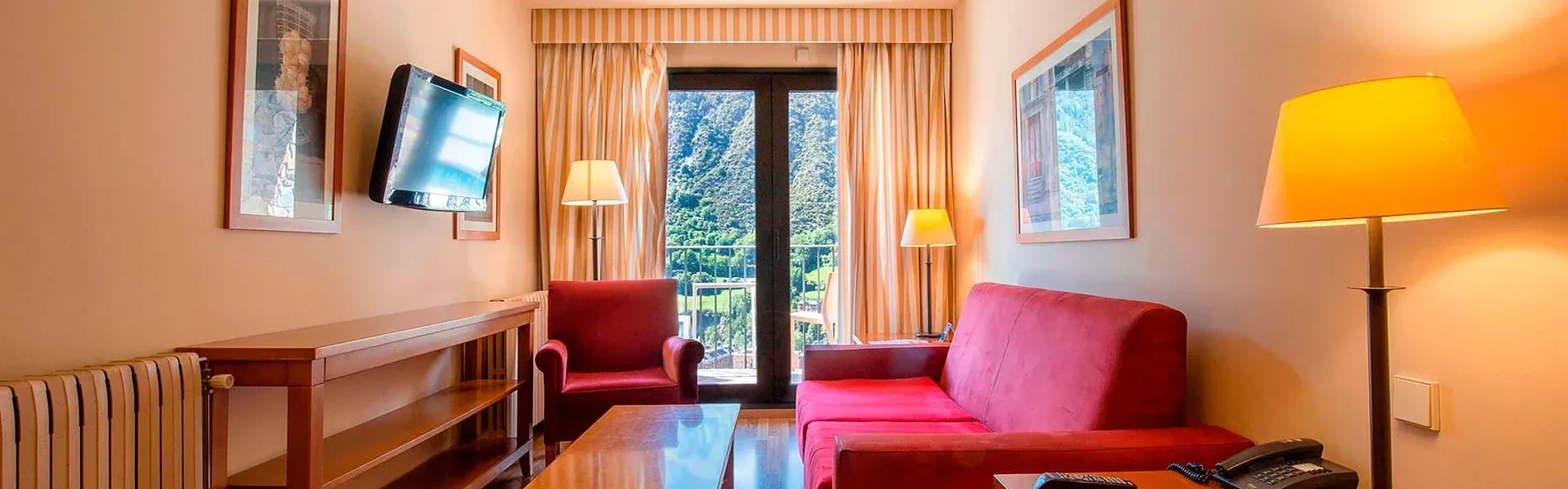 Sofá rojo y sillón frente a balcón con vistas en Apartamentos Shusski.