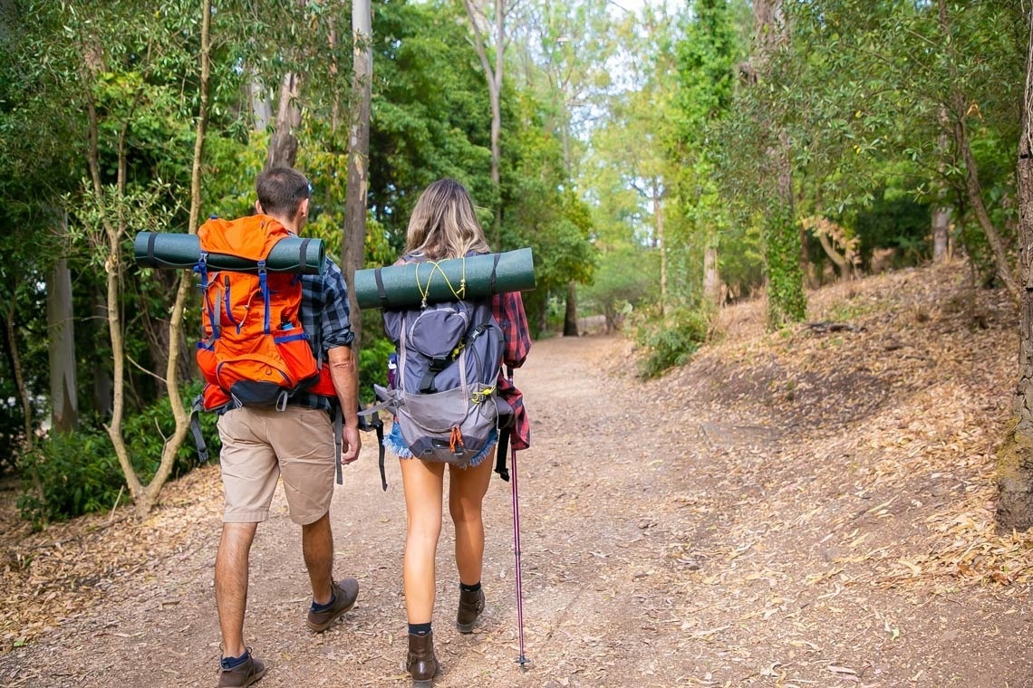 un homme et une femme avec des sacs à dos marchent sur un chemin forestier