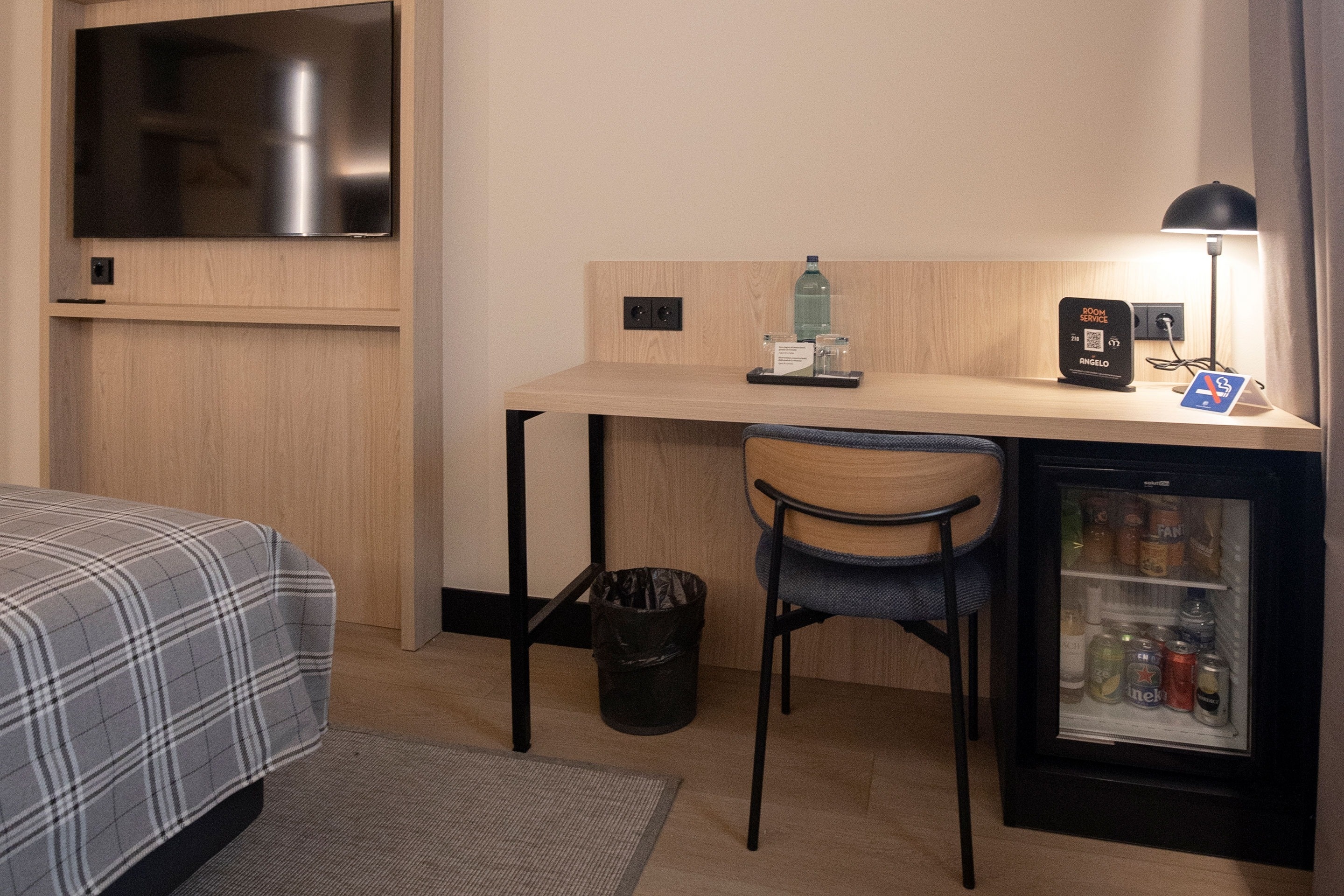 a hotel room with a desk a chair a fridge and a tv