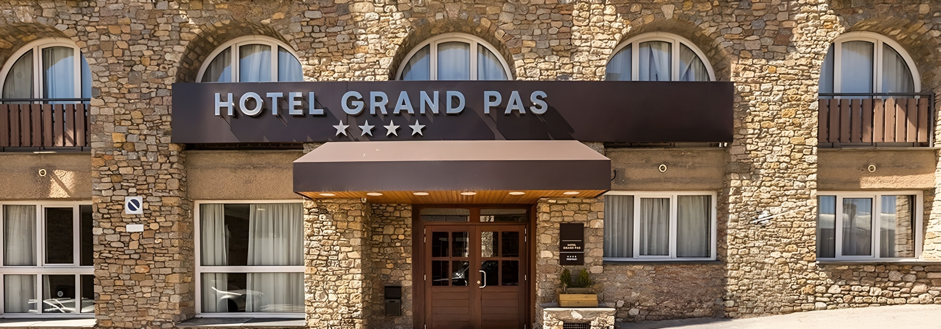 Hotel Grand Pas, façade en pierre 4 étoiles avec entrée, balcons et un skieur.