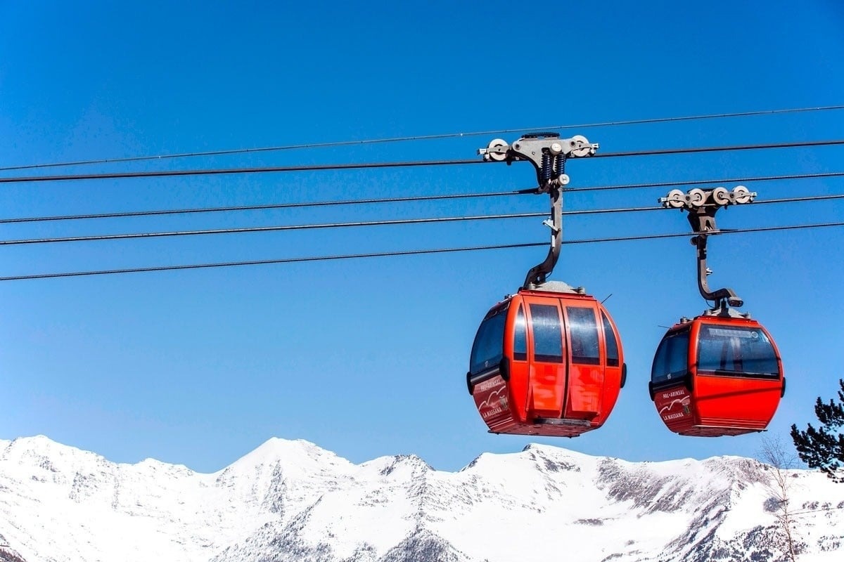 dos góndolas rojas que llevan a los esquiadores a la cima de una montaña cubierta de nieve
