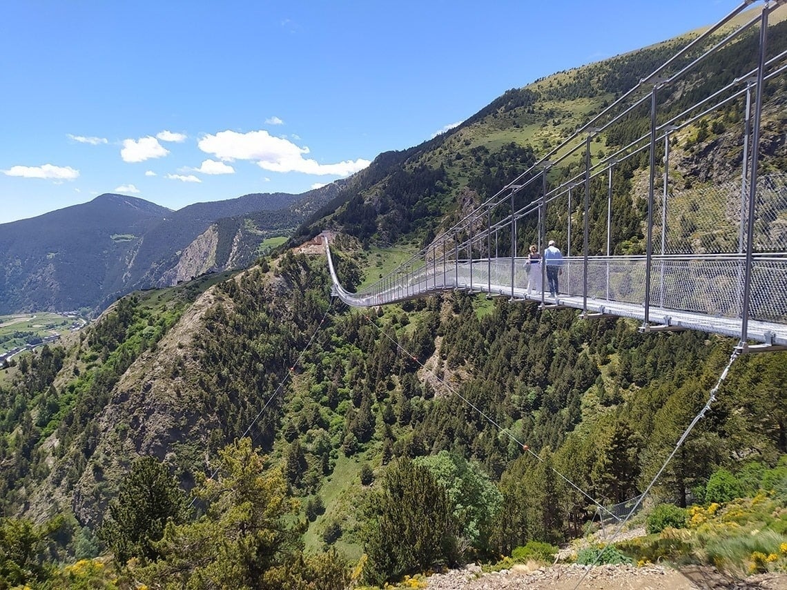 dos personas están en un puente colgante en las montañas