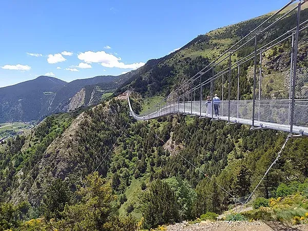 dos personas están en un puente colgante en las montañas