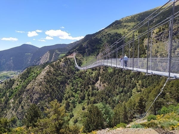 dos personas están en un puente colgante en las montañas