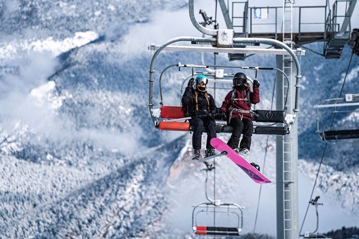 un hombre y una mujer están en un ascensor de esquí con una tabla de snowboard rosa