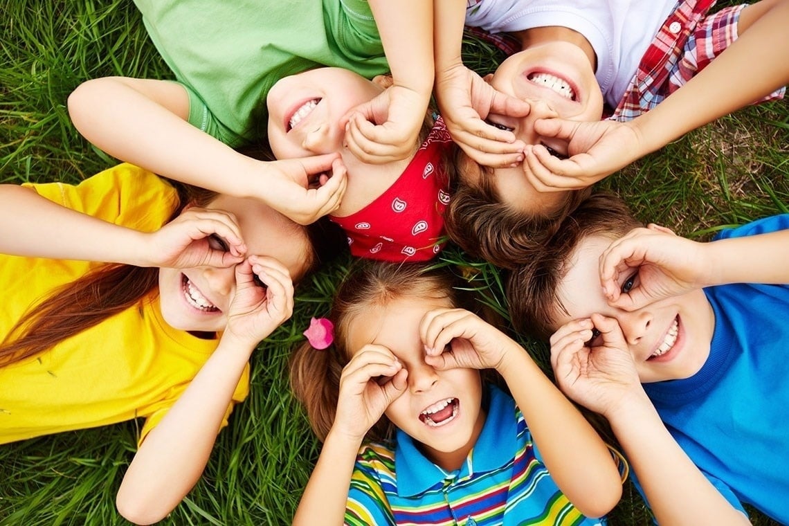 un groupe d' enfants allongés dans l' herbe avec leurs mains devant leurs yeux