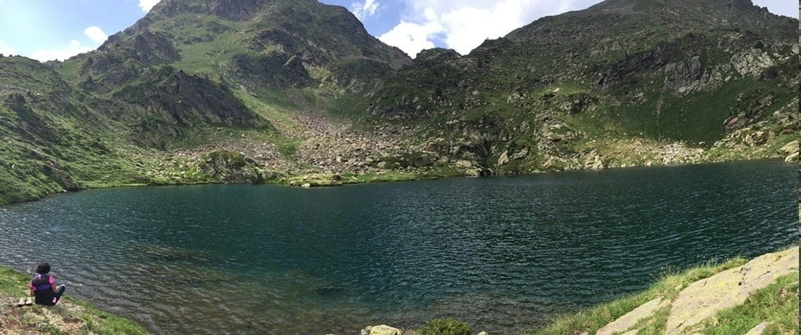 una mujer se sienta en la orilla de un lago rodeado de montañas