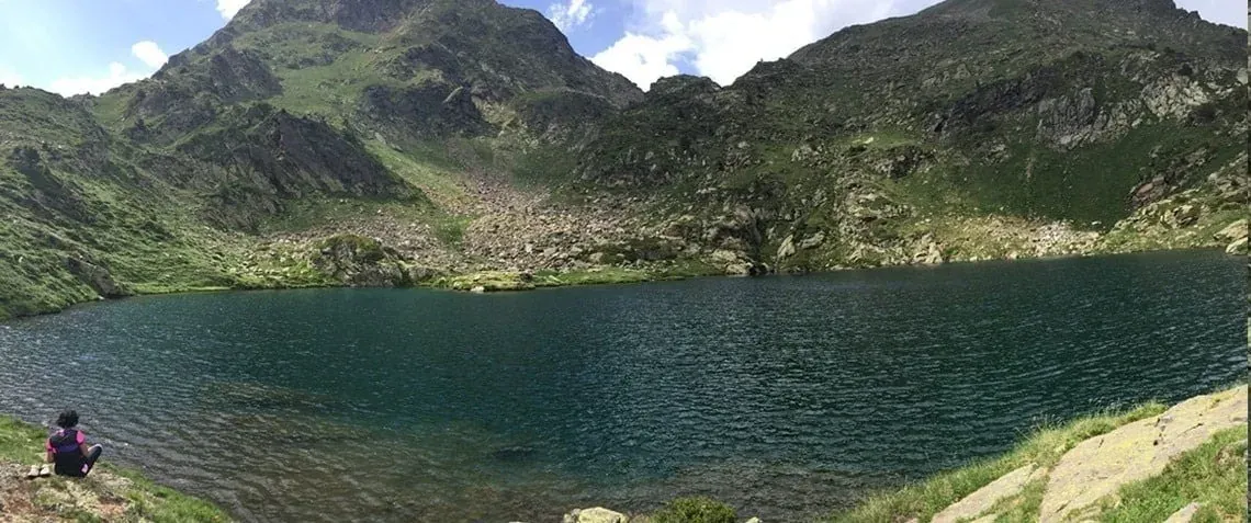 una mujer se sienta en la orilla de un lago rodeado de montañas