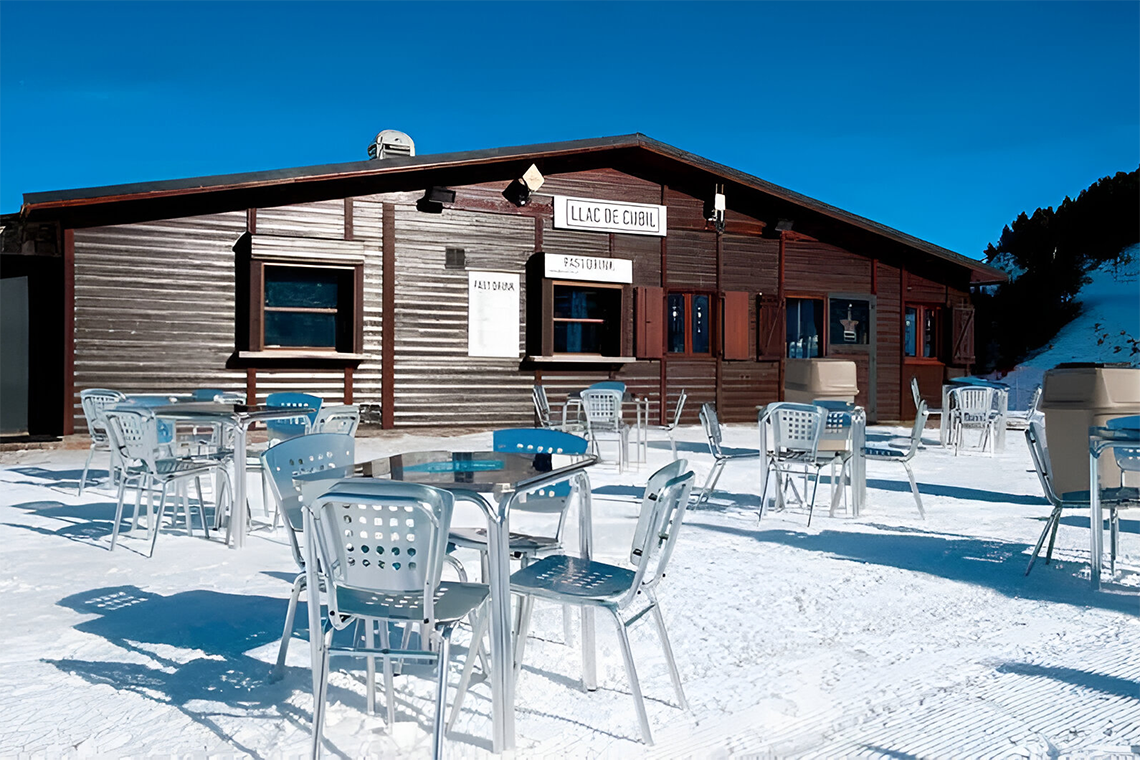 una casa de madera cubierta de nieve con mesas y sillas frente a ella