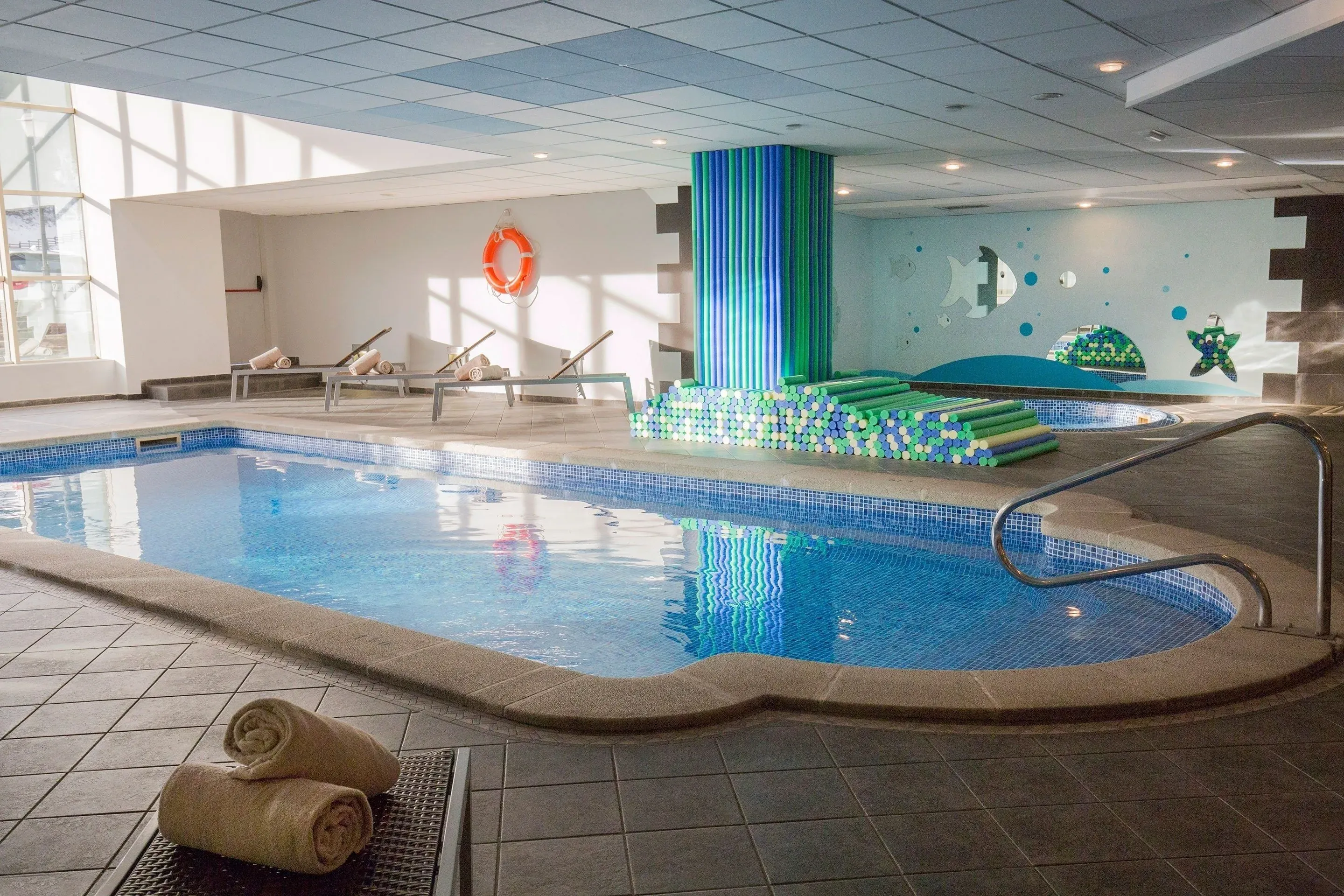 NEXTA: Piscina interior azul con tumbonas y decoración temática de peces.