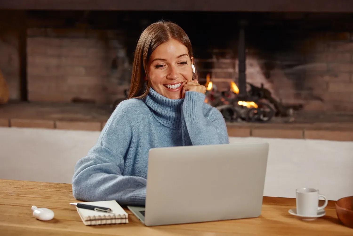 NEXTA: Corporativa. Mujer sonríe en portátil junto a chimenea, sala NEXTA.