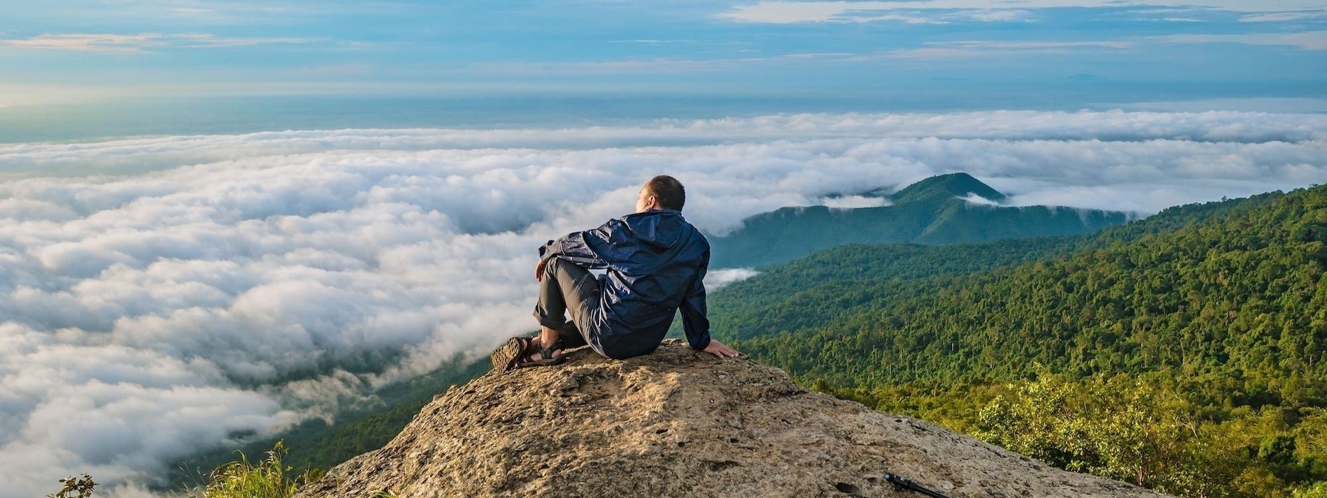 una persona està senta en la cima d' una roca mirant a les nubes
