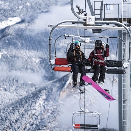 un par de snowboarders montan un ascensor en una montaña cubierta de nieve