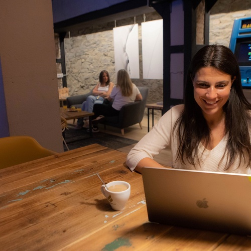 una mujer se sienta en una mesa con una computadora portátil y una taza de café