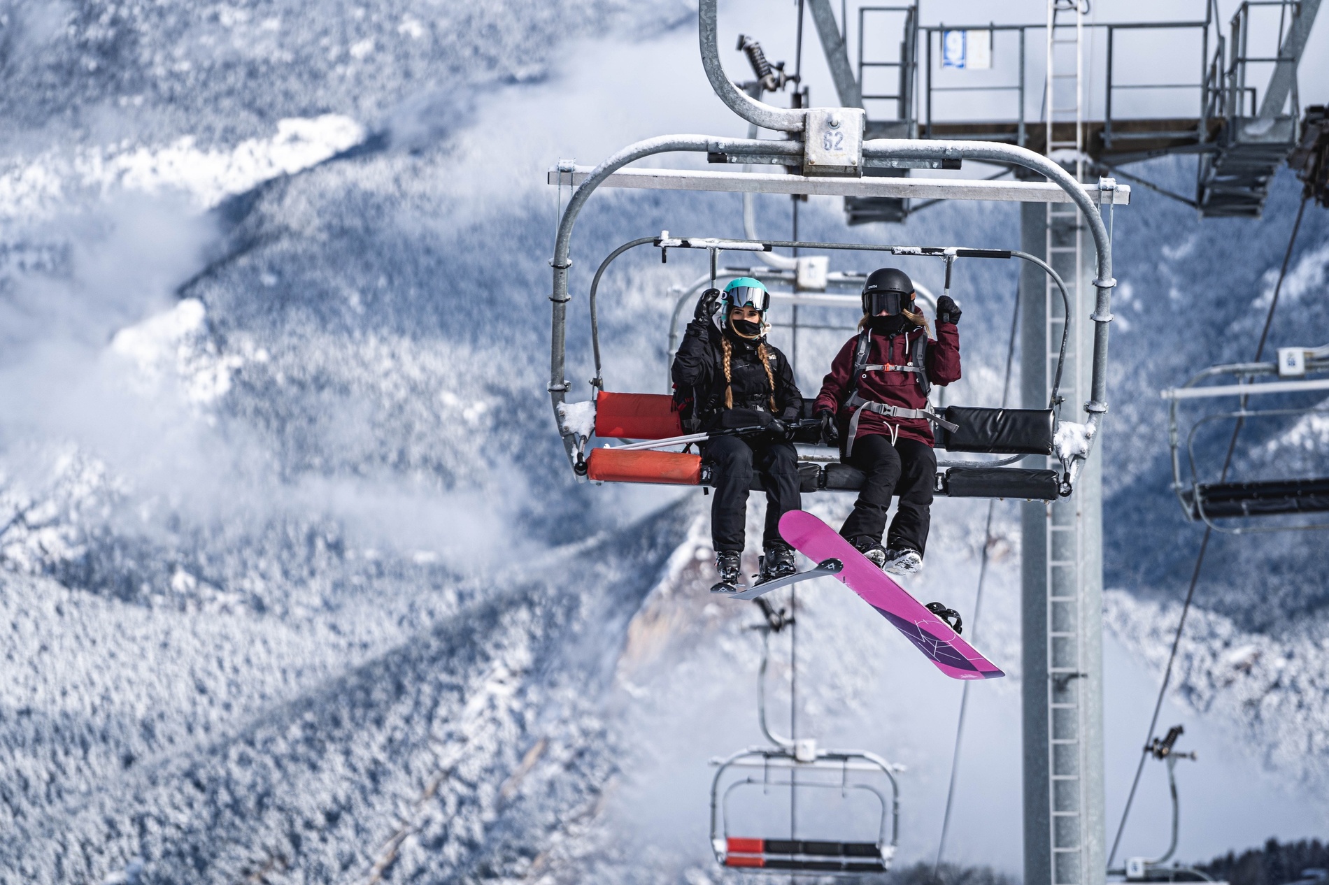 deux skieurs sont assis sur un télésiège avec une planche à neige rose