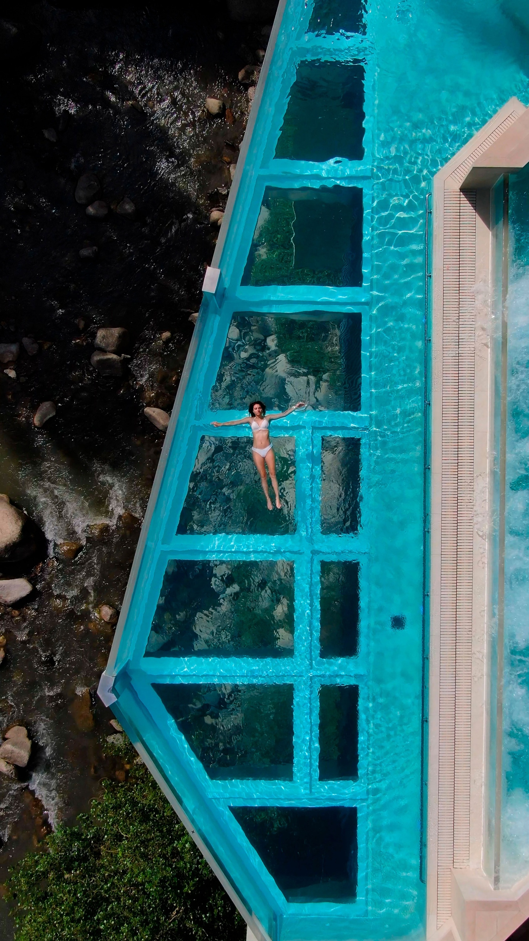 una mujer flota en una piscina transparente junto a un río