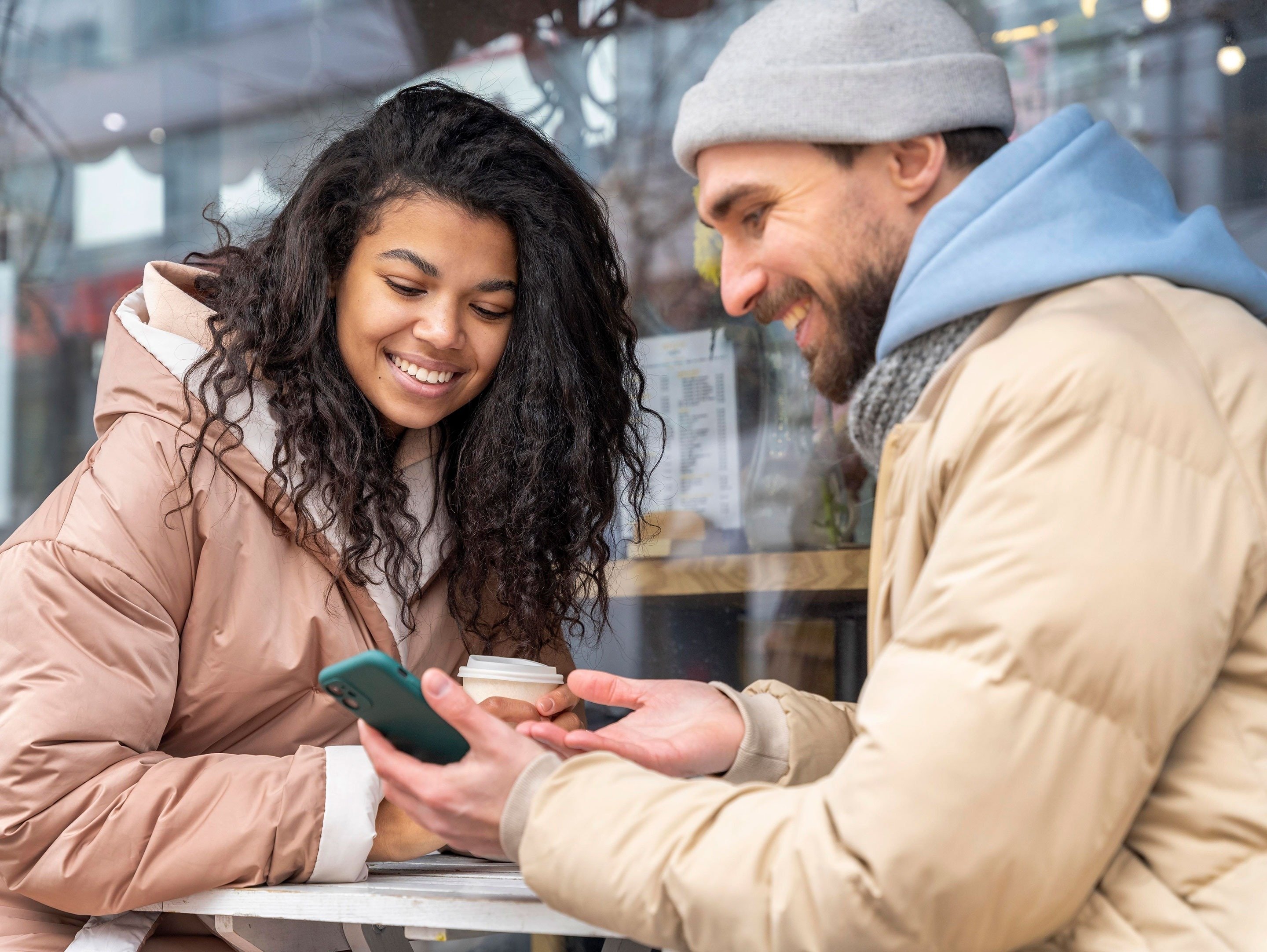 un homme et une femme sont assis à une table et regardent leur téléphone