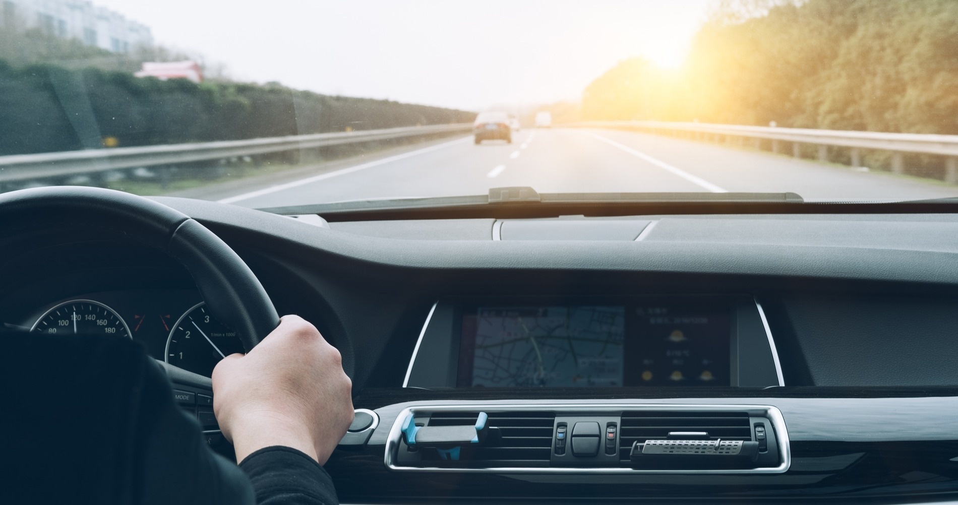 a person is driving a car on a highway with the sun shining through the windshield