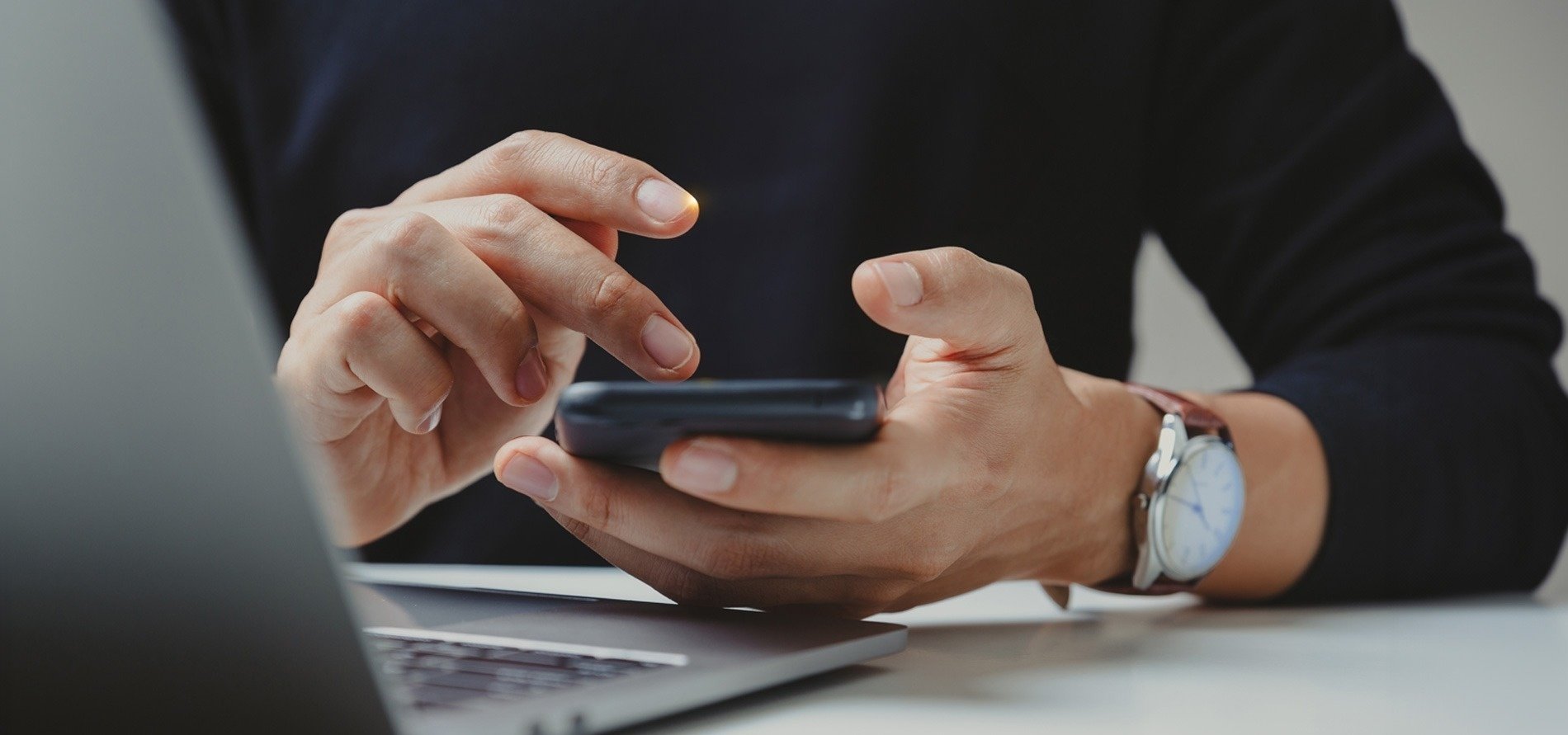 un hombre sostiene un teléfono inteligente frente a una computadora portátil