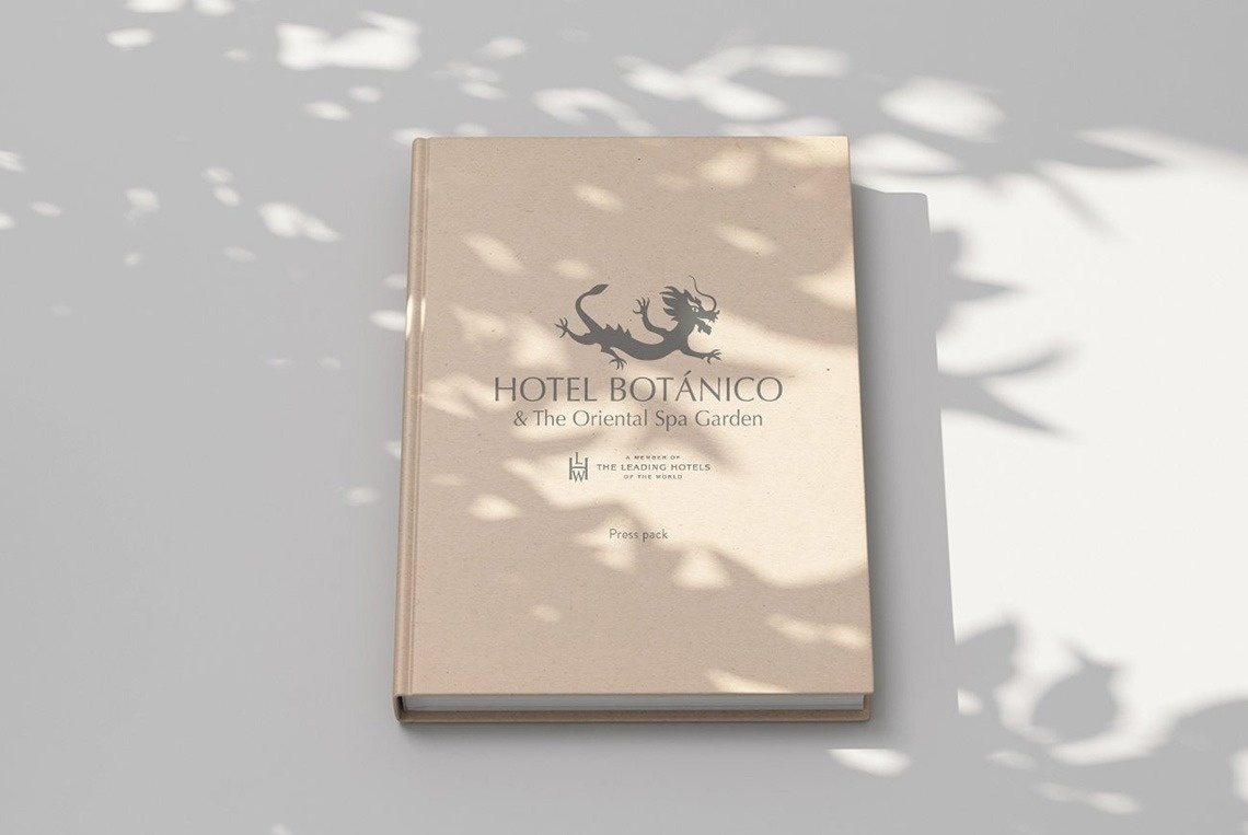 A light brown press pack for "Hotel Botánico & The Oriental Spa Garden" featuring a dragon logo is displayed on a light surface, partially obscured by dappled shadows from foliage.