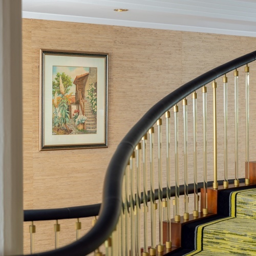 it: Due dipinti raffiguranti teste di cavallo sono appesi a una parete rivestita in paglia, con una ringhiera di scala curva in primo piano sulla destra.