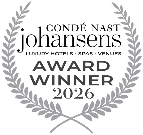 En grå och svart utmärkelseikon visar en lagrarkrans som omger texten "CONDÉ NAST JOHANSENS LUXURY HOTELS · SPAS · VENUES AWARD WINNER 2026" på en svart bakgrund.