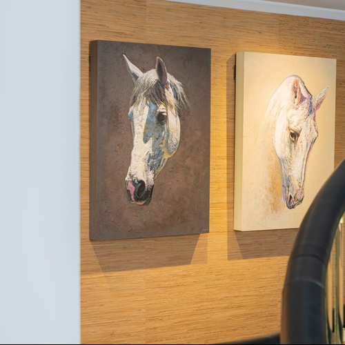 it: Due dipinti raffiguranti teste di cavallo sono appesi a una parete rivestita in paglia, con una ringhiera di scala curva in primo piano sulla destra.