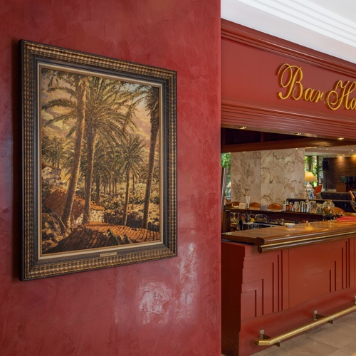 Un vivace interno di bar presenta una parete rossa con un dipinto di palme e un elegante bancone rosso con l'insegna 